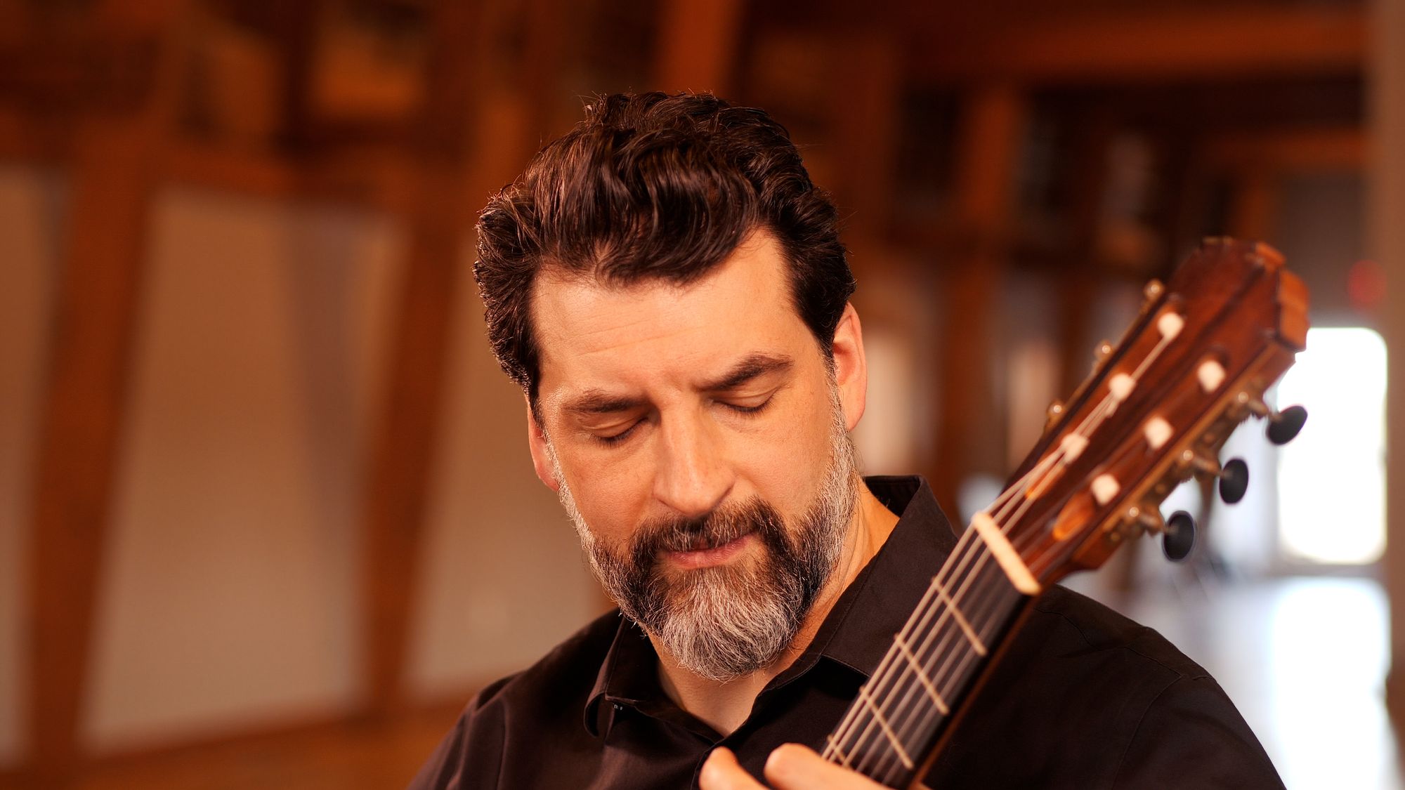Matthew Cochran playing guitar in a timber-framed barn