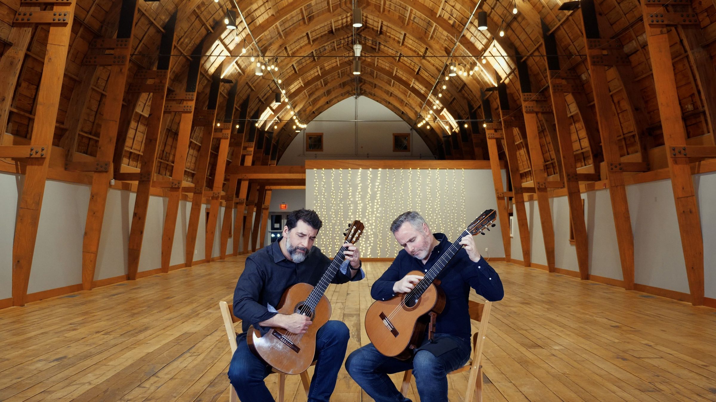 Cochran & McAllister playing guitars in the timber-framed Cathedral Barn