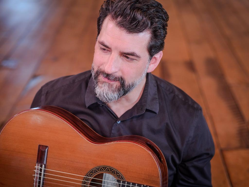 Matthew Cochran with his guitar on a wooden floor